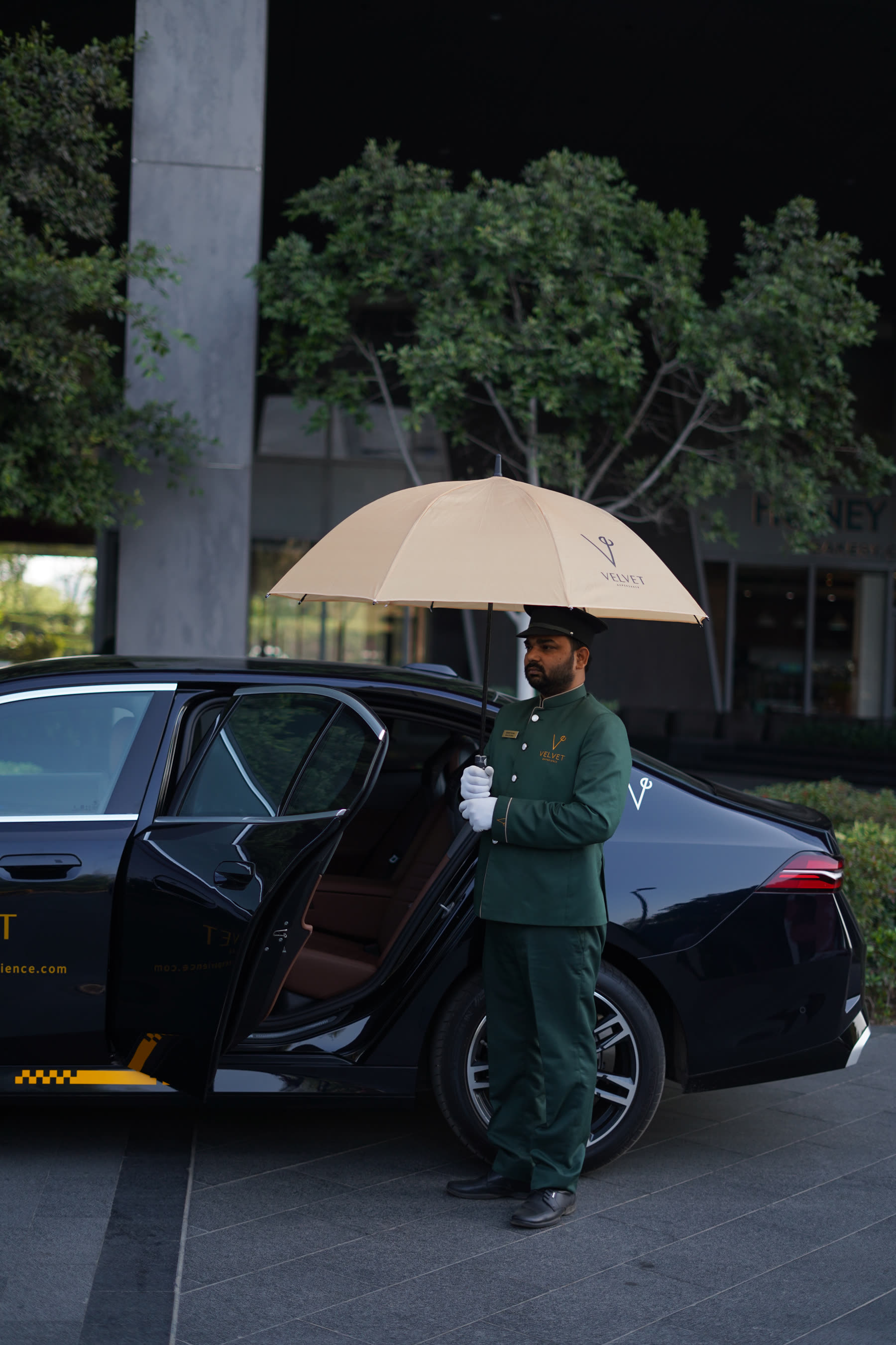 Velvet chauffeur holding an umbrella by an open rear door